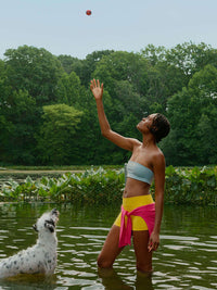 Model wearing Love Bra in a serene lake setting, playing fetch with a dog, showcasing active movement and style.