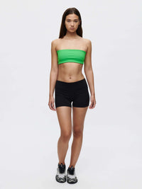 Model showcasing the Love Bra, a low-impact bandeau top in vibrant green, paired with black shorts and sporty shoes.