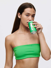 Model wearing the Love Bra in bright green, sipping from a can, showcasing the stylish bandeau design.