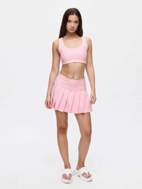 Model wearing a pink top and pleated skirt showcasing the Orbit Bra in a stylish outfit.