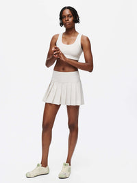 Model showcasing the stylish Orbit Bra paired with a pleated skirt, perfect for medium-impact activities.