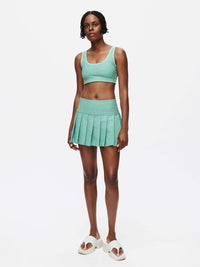 Model wearing Orbit Bra with a matching green pleated skirt, showcasing soft-fit elastic band and OV logo.