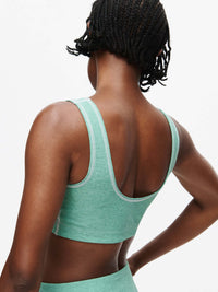 Back view of a model wearing the Orbit Bra in green, showcasing the soft-fit elastic band and textured fabric.