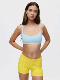 Model wearing a Solar Bra in blue with yellow shorts, showcasing medium support and adjustable straps.