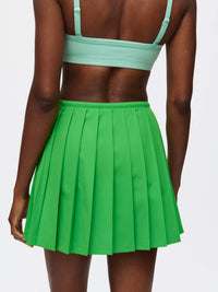 Back view of a model wearing a pleated Stardust Skirt in green with a side zipper and drawstring tie.