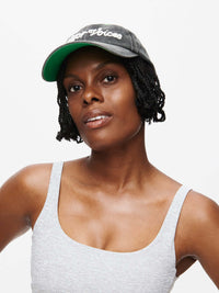 Washed Hat worn by a smiling woman, with the Outdoor Voices signature in stylish topstitching.
