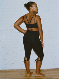 Model in a back pose wearing Apple Bra in Black, with intersecting straps and a plunging neck.