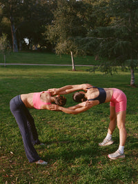 Two models stretching while doing yoga in a park, wearing Double Dip Bra in Cotton Candy and matching shorts.
