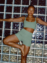 Model in a yoga pose wearing Apple Bra in Sage Green, featuring a plunging neckline and intersecting straps.