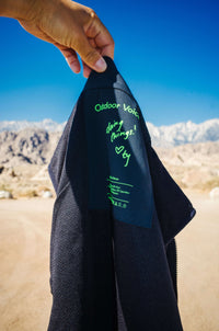 Close-up of the Candy Fleece Vest tag showing Outdoor Voices branding and inspirational message, in natural outdoor setting.