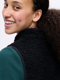 Model smiling in Candy Fleece Vest in Black, showing cozy fabric and mock neck detail.