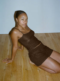 Model sitting in CloudKnit Cami in Brown, featuring a slim fit and feminine neckline, for lounging.