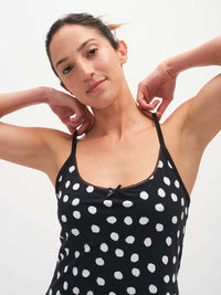Model adjusting straps of Club Dress in Black with white polka dots, featuring picot trim and a cute bow.