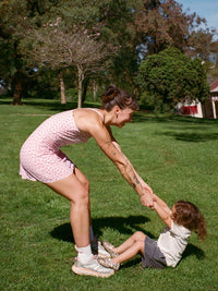 Model playing with child in Club Dress, light pink pattern, enjoying a sunny day in the park.