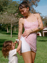 Model wearing Club Dress in White with floral print, showing adjustable straps and playful moment with child.