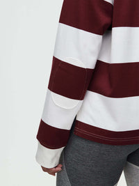 Back view of a woman wearing a Club Polo with maroon and white stripes, with the ribbed cuffs.