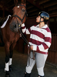 Model wearing a Club Polo in stripes, grooming a horse in a stable setting, with comfort and style.