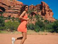 Model running in Doing Things Dress in Coral, showing a sporty fit for outdoor activities.