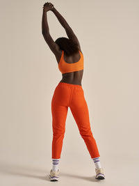 Model stretching in back view of Double Time Bra in Orange, snug fit for active wear.