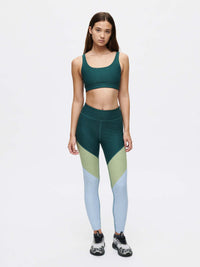 Model wearing Double Time Bra in Dark Green with medium support, paired with color-blocked leggings.