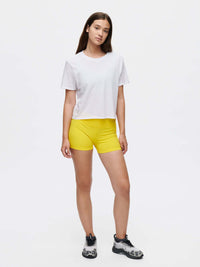 Model standing in relaxed pose wearing Everyday Shortsleeve in White, featuring a slight crop and paired with yellow shorts.