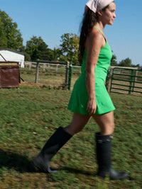 Woman wearing The Exercise Dress in a vibrant green while walking on a farm with rubber boots.