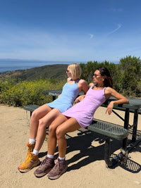 Two models wearing The Exercise Dress in Light Blue and Lilac, enjoying the outdoors with adjustable straps.