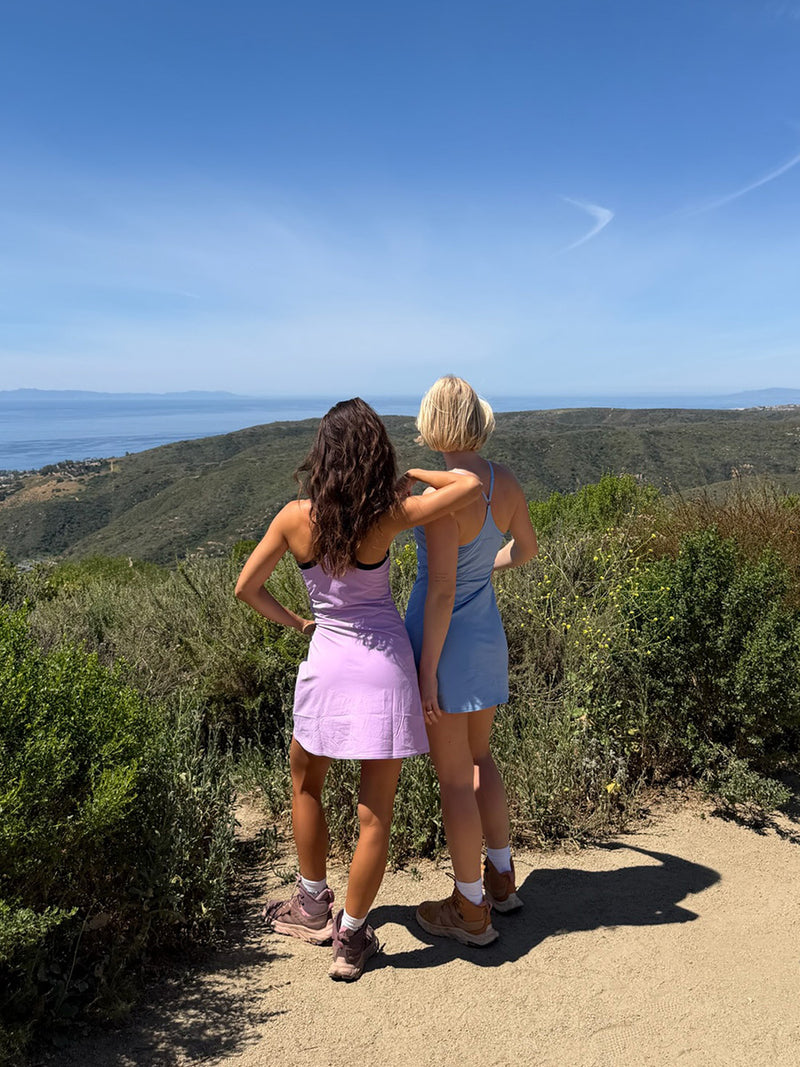 Models standing outdoors wearing The Exercise Dress in Lavender and Blue, with a scenic landscape view.
