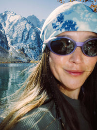 Model smiling by a lake wearing Frosted Beanie, exclusive Elf Garden print, and stylish sunglasses.