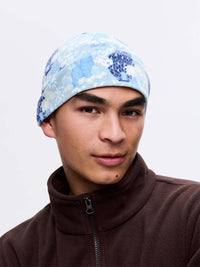 Model wearing Frosted Beanie in blue with exclusive Elf Garden print featuring pine trees and daisies.