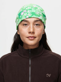 Model wearing Frosted Beanie in Green, featuring a floral print of pine trees and daisies.