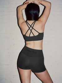 Back view of model wearing Gemini High Rise Short in Black, with the wide waistband and cross-back detailing.