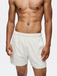 Model standing in High Stride 5" Short with Pockets in light beige, with the lightweight training design.