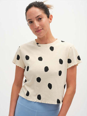 Model smiling, wearing Polka Tee in cream with playful black polka dots and a lettuce edge finish.
