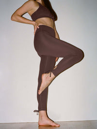 Model posing in Puddle Legging in dark brown, featuring adjustable ties at the ankle for a customized fit.