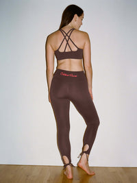 Model in back view wearing Puddle Legging in Brown with keyhole cut outs at the leg and adjustable ties.