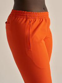 Side view of model wearing RecTrek 26" Pant in vibrant orange with a stylish zip pocket for convenience.