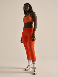 Model standing confidently in RecTrek 26" Pant in vibrant orange, with 4-way stretch for mobility.