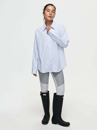 Model standing in Striped Sun Shirt, oversized fit in light blue, paired with performance leggings and rubber boots.