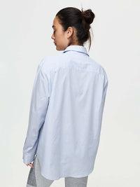 Rear view of model wearing Striped Sun Shirt in light blue, featuring subtle stripes and an oversized fit.