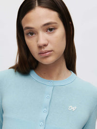 Close-up of model wearing Sugar Cardigan in soft blue, featuring hand-embroidered OV signature detail.