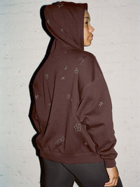 Model in profile wearing Sunny Hoodie in Dark Brown, featuring whimsical embroidered designs on soft fleece.
