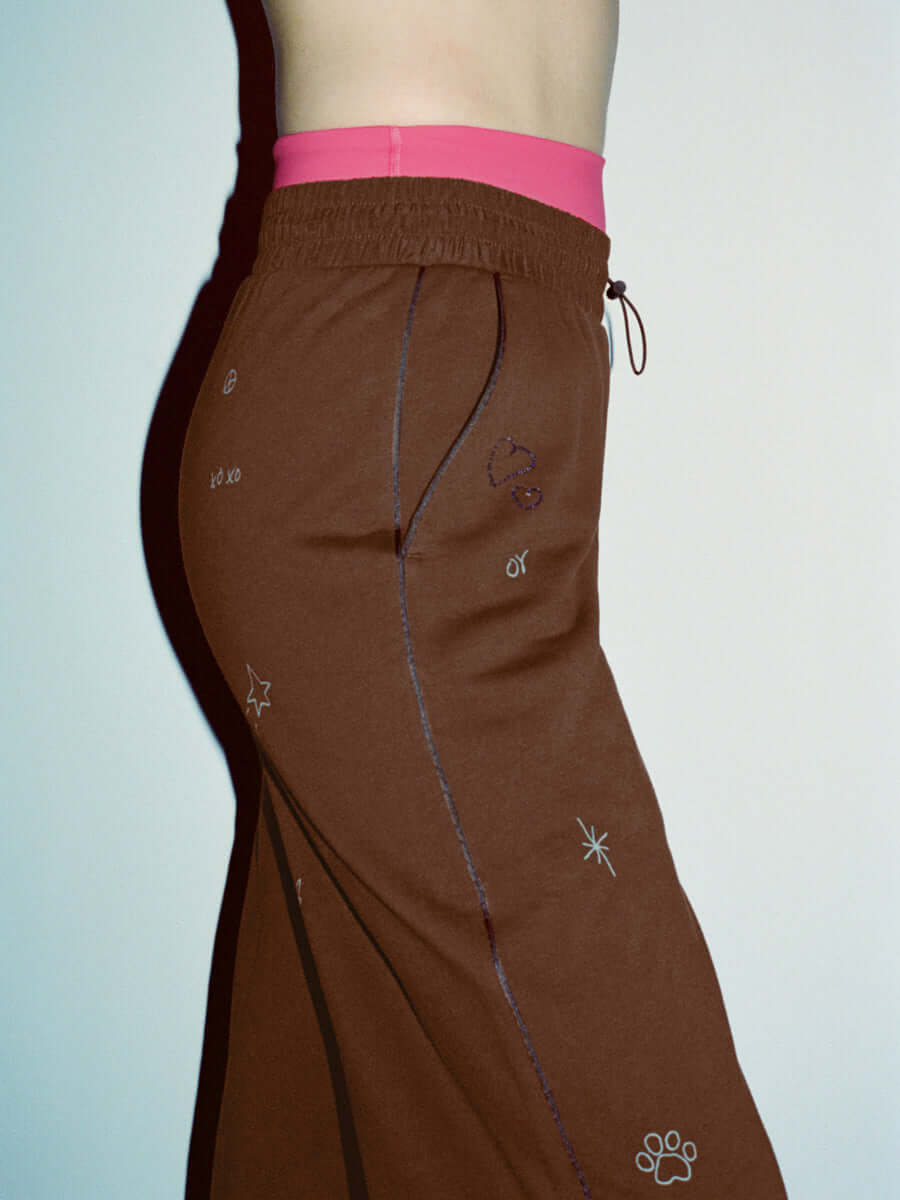 Side view of Sunny Sweatpant in Brown with a technical nylon waistband and fun embroidered details.