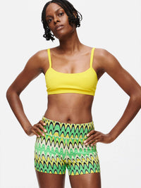 Model with the TechSweat 3" Short in a vibrant pattern, paired with a yellow crop top for a sporty look.