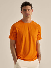 Model standing in ThinkFast Mesh Shortsleeve in orange, featuring a breathable fabric for activewear.