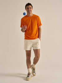 Model playing with a ball in ThinkFast Mesh Shortsleeve in Bright Orange, featuring a breathable design for active movement.
