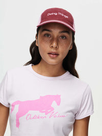 Model wearing a Doing Things Trucker Hat with a pink graphic tee, with a casual outdoor style.