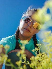 Model with braids wearing Waffle Baby Tee in Aqua, enjoying nature with sunglasses and flowers in the foreground.