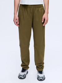 Model standing in Zephyr 29" Pant in Olive, featuring zippered pockets and a drawstring waist.