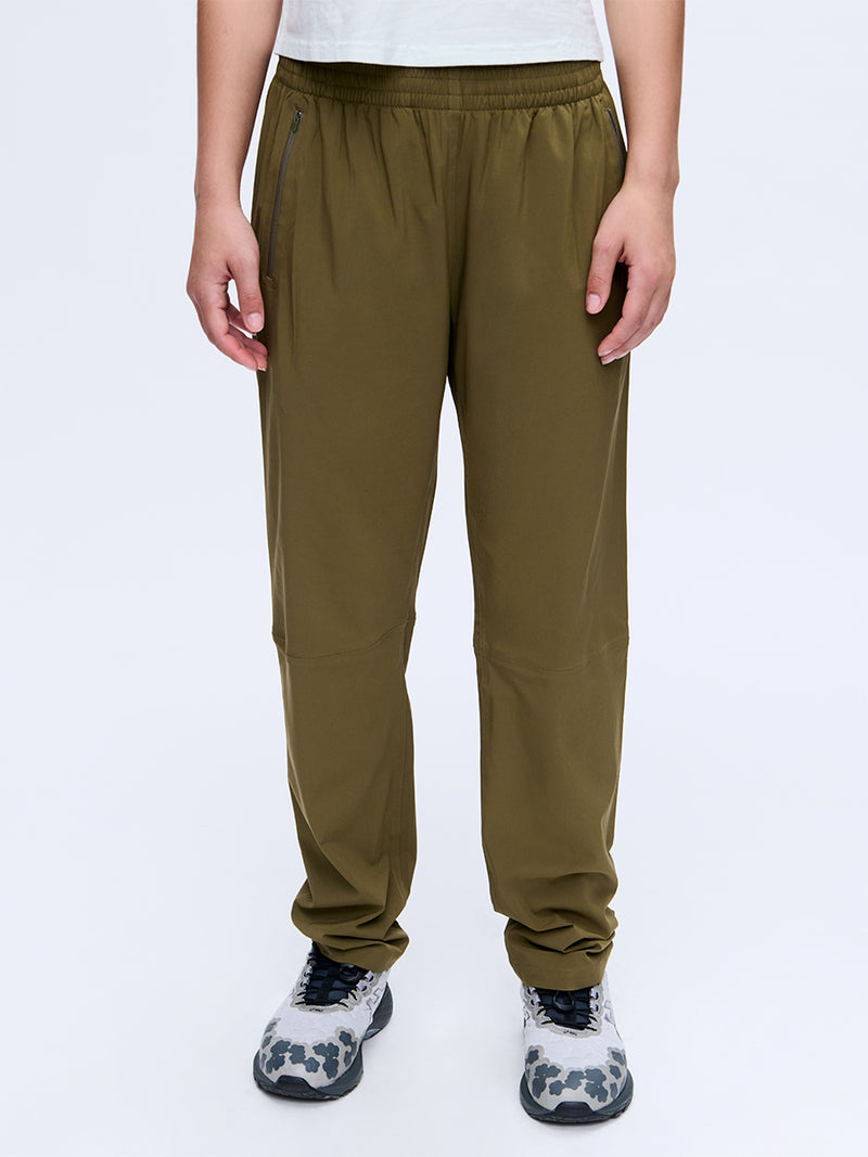Model standing in Zephyr 29" Pant in Olive, featuring zippered pockets and a drawstring waist.